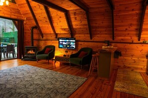 Ein gemütlicher Raum mit Holzwänden, einem Kamin, zwei Sesseln, einem Fernseher und einem Holzboden.