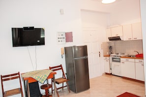 A compact kitchen with a refrigerator, stove, oven, and a dining area with a table and chairs. - Arcadia Coastal Studio by ΜΡS (ΑΡΚΑΔΙΑ)