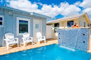 A swimming pool with two white chairs, a tiled pool area, and a building with a clock and a lifebuoy.