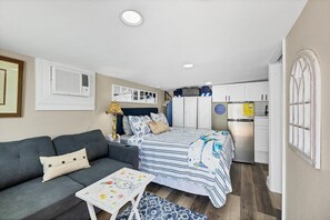 A compact room with a bed, a sofa, a small table, a kitchenette, and a window.