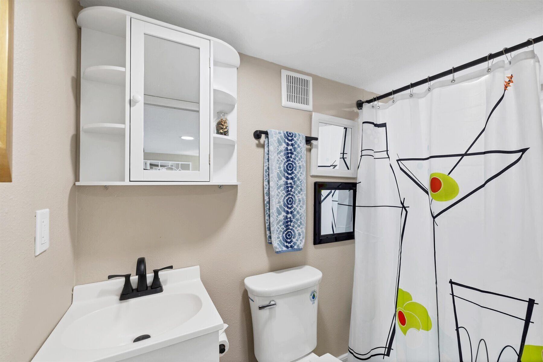 A bathroom with a white sink, toilet, and cabinet, a shower curtain with a geometric pattern, and a towel hanging on the wall.