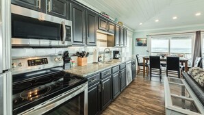 A kitchen with a built-in microwave, stove, and sink, a dining area with a table and chairs, and a view through a glass door. - Direct Beach Access Classic Surfside Home (Surfside Beach)