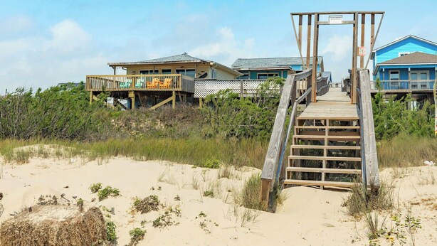 A beach house with a wooden deck leading to a porch, surrounded by sand and vegetation. - Direct Beach Access Classic Surfside Home (Surfside Beach)