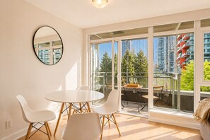 A modern room with a round table, white chairs, a large window with a view of buildings and trees, and a round mirror on the wall. - Yaletown, A/C, parking, 7 min walk to beach, downtown, Skytrain (Vancouver)