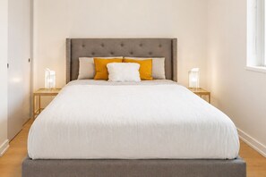 A neatly made bed with a grey upholstered headboard, two bedside tables with lamps, and a window with a view. - Yaletown, A/C, parking, 7 min walk to beach, downtown, Skytrain (Vancouver)