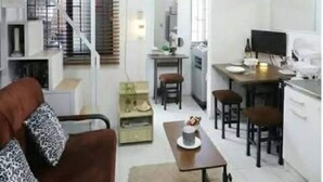 Un espace de vie compact comprenant un canapé, une table à manger, des chaises, un coin cuisine et un escalier.