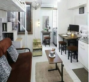 A compact living space with a sofa, dining table, chairs, kitchenette, and a staircase. - One Metropolitan Place (Pasay City)