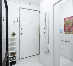 A white door with a keyhole, a small plant, and a shoe rack with shoes. - One Metropolitan Place (Pasay City)