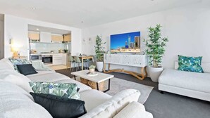 Una sala de estar moderna con un sofá, una mesa de centro y un televisor. Se ve una cocina al fondo.