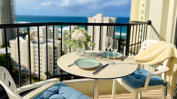 Un balcone con un tavolo apparecchiato per due, un vaso con fiori e vista sull'oceano.