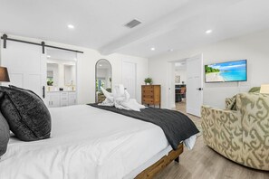 Ein Schlafzimmer mit Bett, Kommode, Fernseher und Blick auf einen Strand.