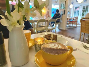 A dining table with a yellow cup of coffee, a slice of cake, and a vase with white flowers. - Quiet River 1BR Hideaway (Surfers Paradise)