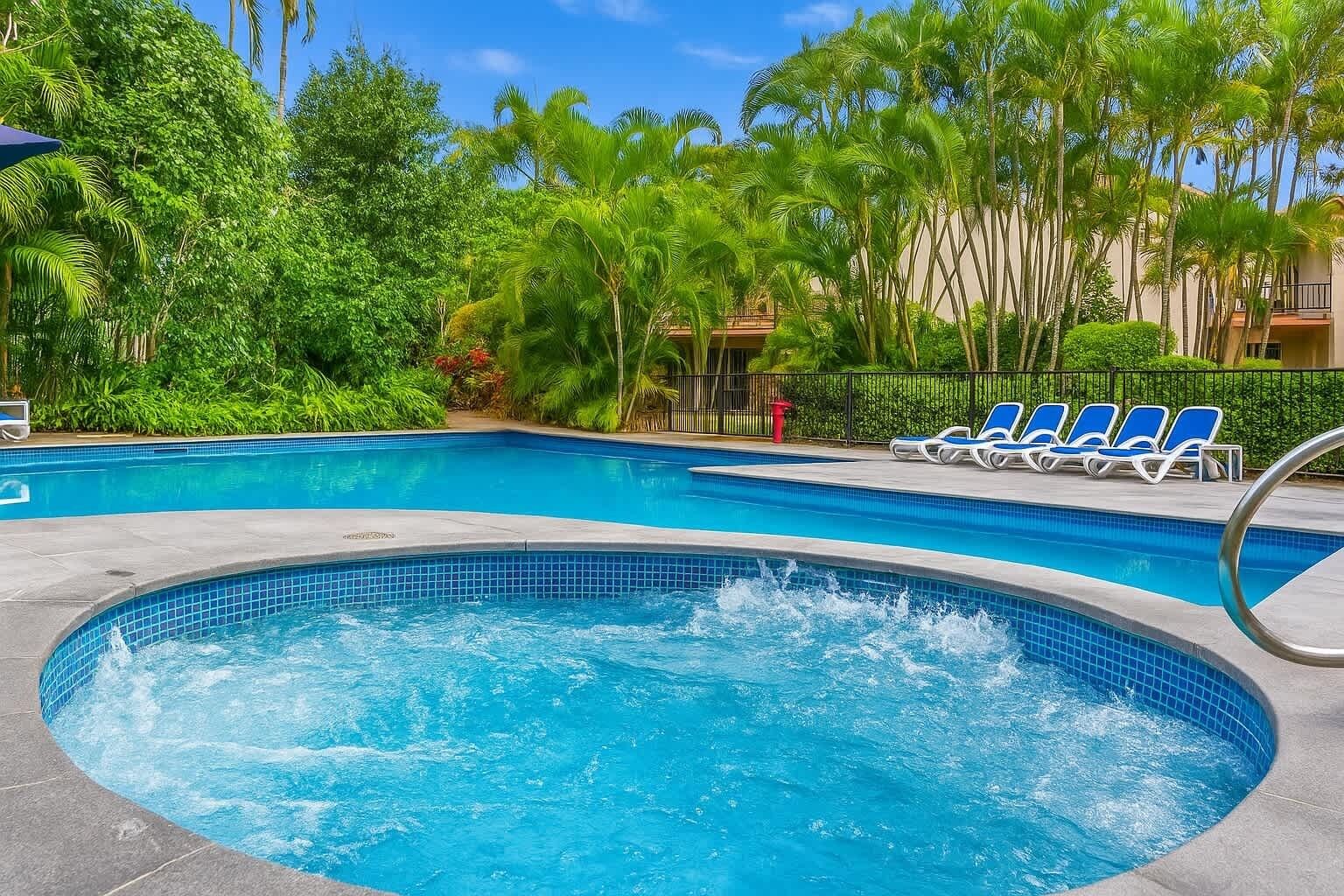 Une piscine avec un jacuzzi, entourée de palmiers et de chaises longues.