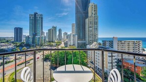 Ein Balkon mit Tisch und Stühlen, der auf einen Stadtblick mit hohen Gebäuden und den Blick auf das Meer bietet.