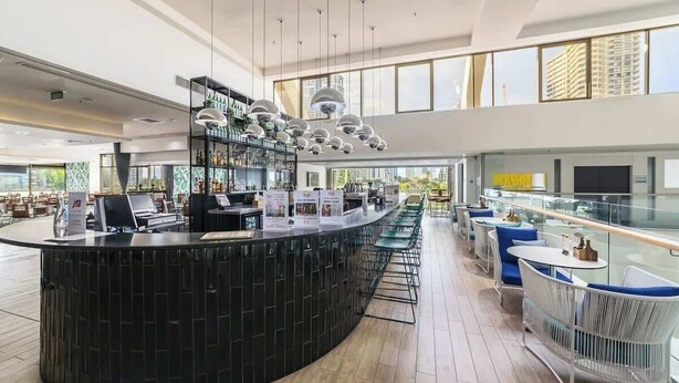 Eine moderne Bar mit einer gebogenen Theke, mehreren Pendelleuchten und Blick auf die Stadt durch große Fenster.