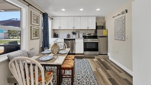 A compact kitchen with white cabinets, a dining table set with plates and glasses, and a patterned rug.