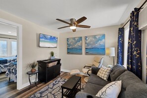 Ein Wohnzimmer mit Deckenventilator, einer Couch, einem Fernseher und Kunstwerken an der Wand.