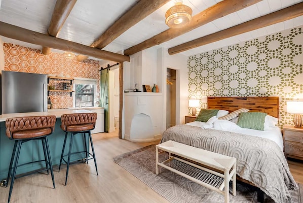 A room with a bed, a bench, a bar area with stools, and a kitchen.