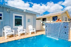 A swimming pool with two white chairs, a tiled pool area, and a building with a clock and a lifebuoy.
