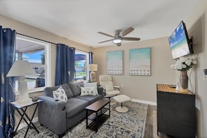 A living room with a gray sofa, a coffee table, a chair, a TV, and artwork on the wall.