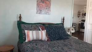 A bed with patterned bedding, a wall-mounted painting, and a bedside table.