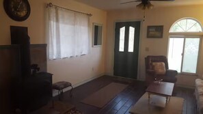 A living room with a dark wooden floor, a sofa, a coffee table, a chair, a clock, and a door with windows.