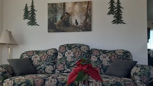 A living room with a floral sofa, a vase with flowers, and a painting of a forest scene.