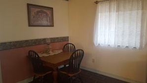 A dining area with a table and chairs, a framed picture on the wall, and a window with curtains.