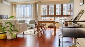 A modern living room with a sofa, chairs, a dining table, and a kitchen area with a window view. - Refuge in Funchal II, a Home in Madeira (Funchal)