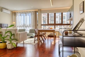 Ein modernes Wohnzimmer mit Sofa, Sesseln, einem Esstisch und einer Küchenzeile mit Blick aus dem Fenster.