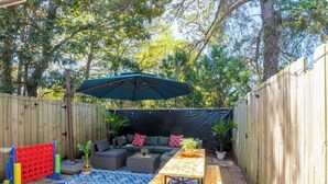 A backyard with a wooden fence, a blue patterned rug, a wooden table, a bench, a sofa, and an umbrella. - Wonderful 2-bedroom townhome close to beach +Pool (Myrtle Beach)