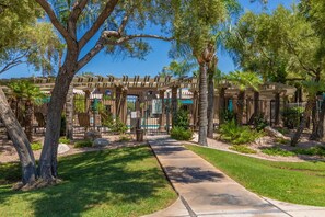 Ein überdachter Außenbereich mit einer Pergola, Palmen und einem Weg zum Pool.