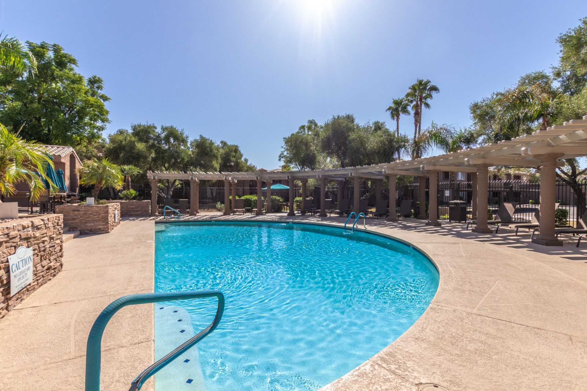 A swimming pool with a clear blue water, surrounded by a covered patio area with chairs and umbrellas.