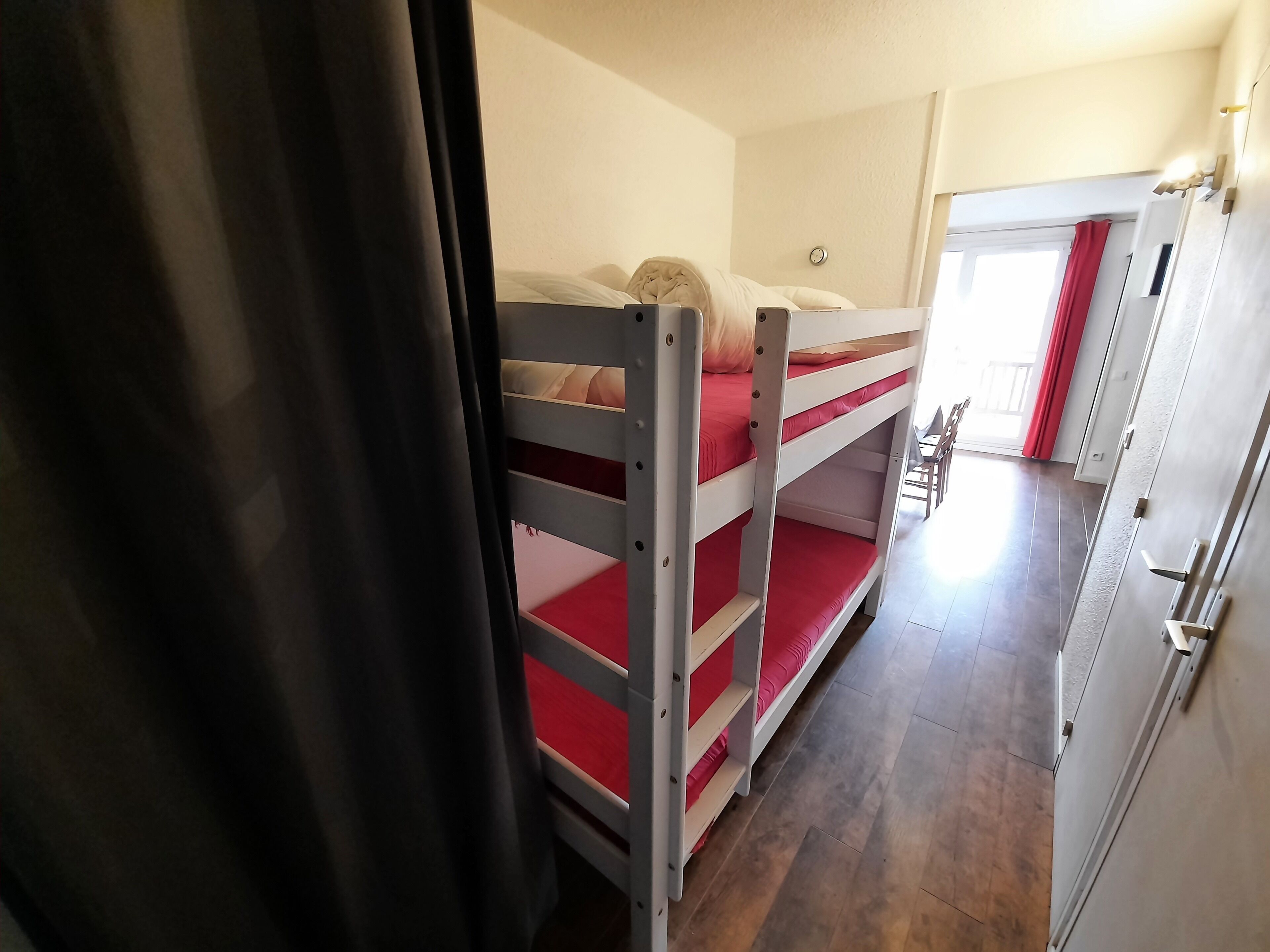 A bunk bed with red bedding, a wooden floor, and a door with a handle.