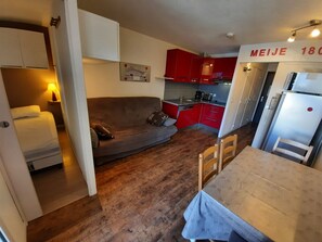 Ein kompakter Wohnraum mit einer Couch, einem Esstisch, einer Küchenzeile mit roten Schränken und einem Kühlschrank.