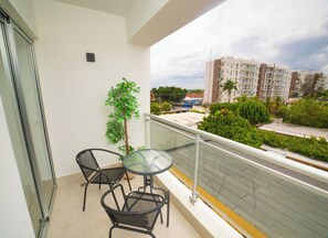 Un balcón con una mesa y sillas de vidrio, una planta en maceta y vistas a edificios y áreas verdes.
