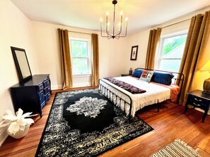 Ein Schlafzimmer mit einem großen Bett, einer Chandelüster, einem Schminktisch und einem Fenster mit Vorhängen.