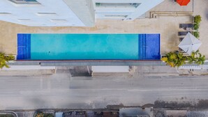 An aerial view of a swimming pool with a tiled deck, surrounded by outdoor seating and palm trees. - Majestuoso Apartamento 2 habitaciones  (Boca Chica)