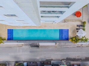 Luftaufnahme eines Schwimmbeckens mit Fliesen umgeben von Sitzgelegenheiten im Freien und Palmen.