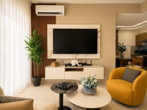 Ein modernes Wohnzimmer mit Flachbildfernseher, einer Couch, einem Couchtisch und einer Zimmerpflanze.