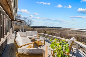 Eine Terrasse mit Sofa, Stühlen und Tisch, mit Blick auf eine Küstenlandschaft.