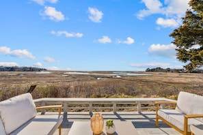 Varanda com duas cadeiras brancas acolchoadas e uma mesa, com vista para uma paisagem natural com corpos d'água e árvores.