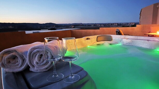 Un bain à remous avec un éclairage vert, un foyer et des serviettes et des verres disposés sur une table.