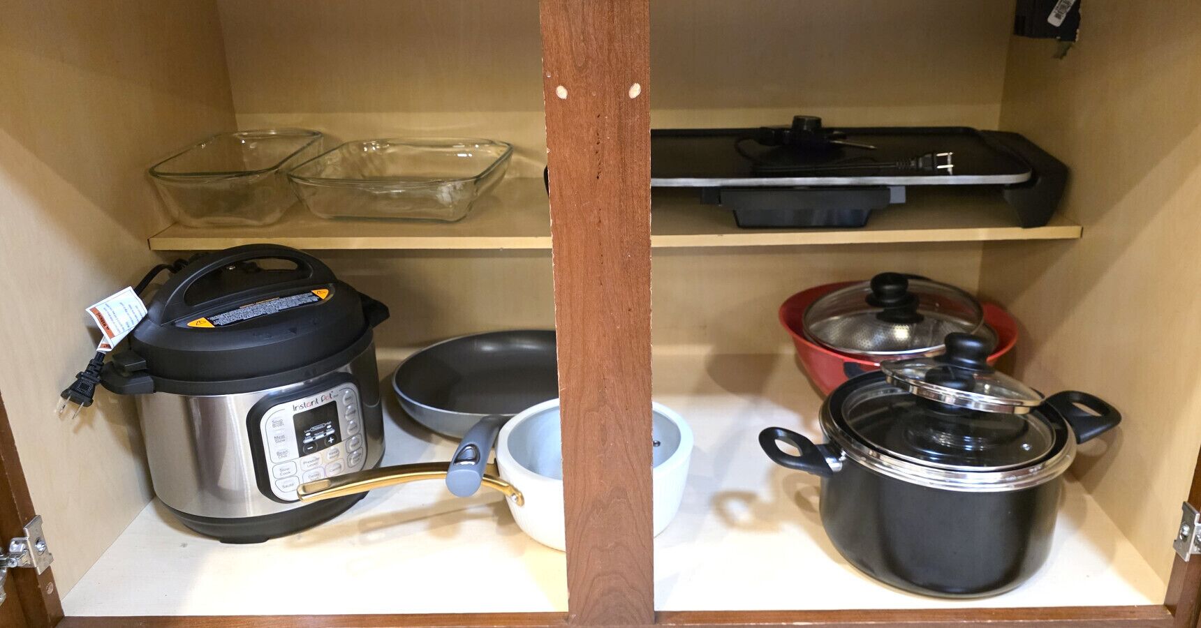 Et køkken med indbygget ovn, riskoger, pande, gryde og en glas bageform.