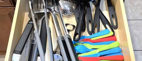 Eine Schublade mit verschiedenen Küchenutensilien, darunter Pfannenwender, Zangen und bunte Plastikbesteck.