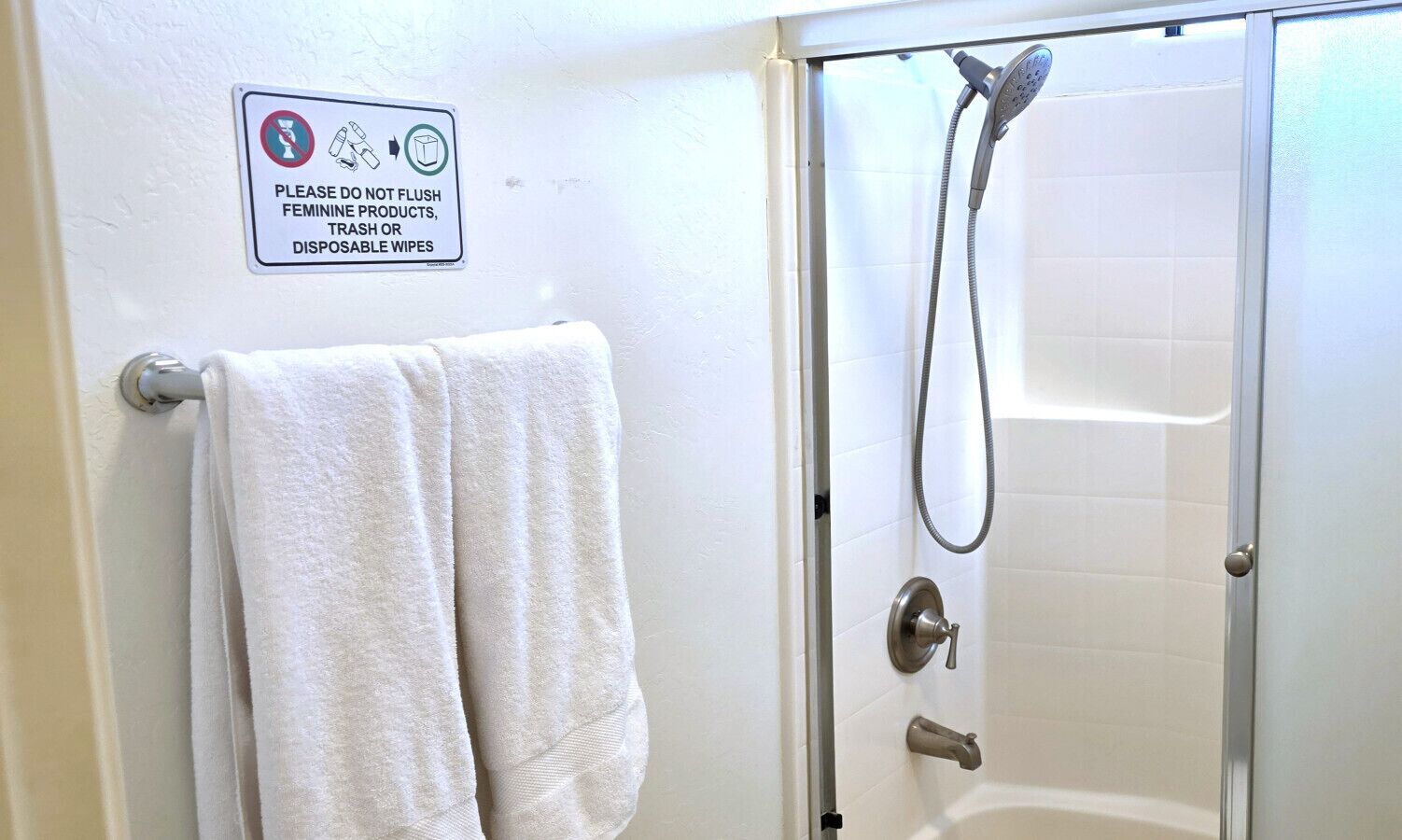A bathroom with a shower, a towel rack, and a sign prohibiting flushing feminine products.