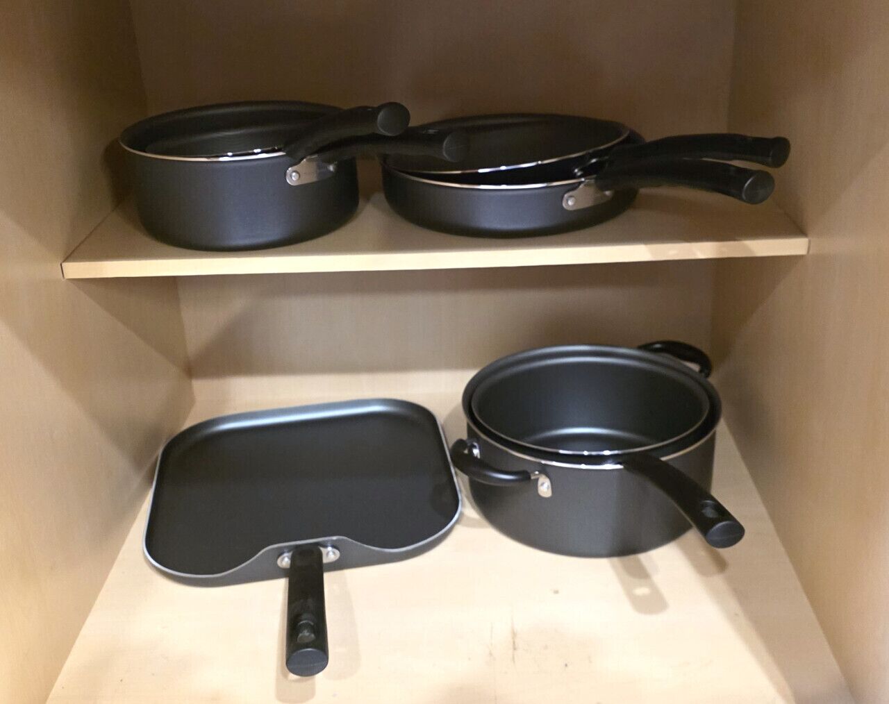 A kitchen shelf with three black pans and a black frying pan.