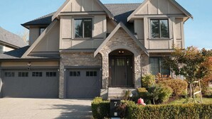 A two-story house with a stone facade, a central entrance, and two garages. - Bright 3BR Langley Home | Ensuite + Office + Parking (Langley Township)