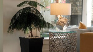A room with a large window, a framed picture of Osborne House, a potted plant, a lamp, and a round table with a glass top. - Bright 3BR Langley Home | Ensuite + Office + Parking (Langley Township)