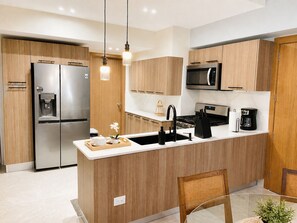 A modern kitchen with wooden cabinets, stainless steel appliances, a central island, and pendant lighting. - Apartamento bellísimo y nuevo (Boca Chica)